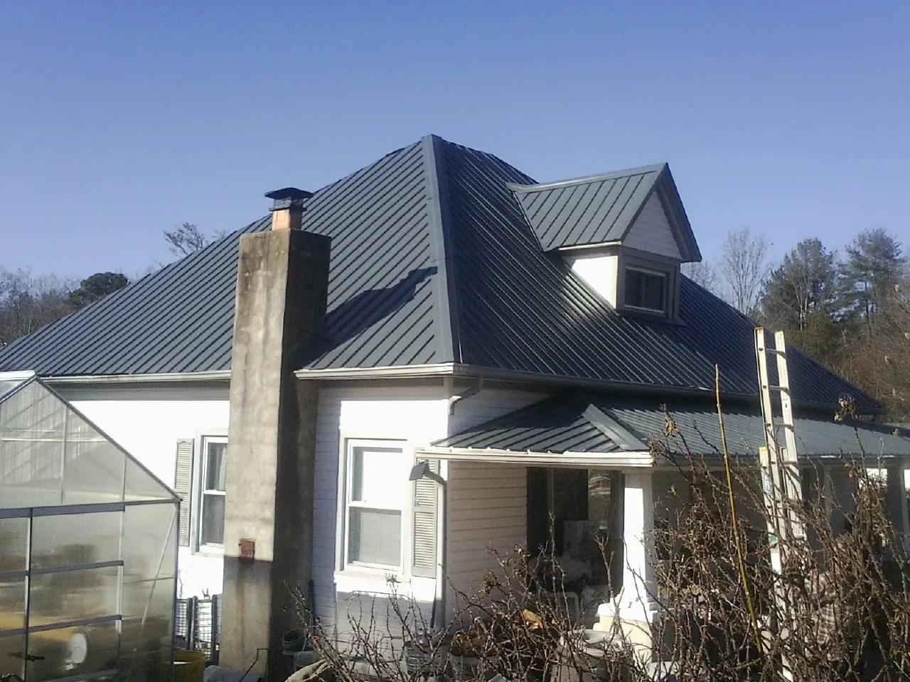 Dark blue standing seam metal roof on a white farmhouse with dormer — Slate & Tile Roof Repair by Roofing Brothers in Petoskey