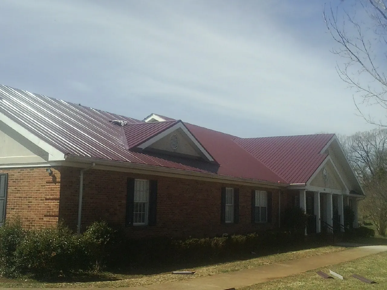 Red metal roof with gabled entries on a long brick building, from a Hail Damage Roof Repair job in Petoskey