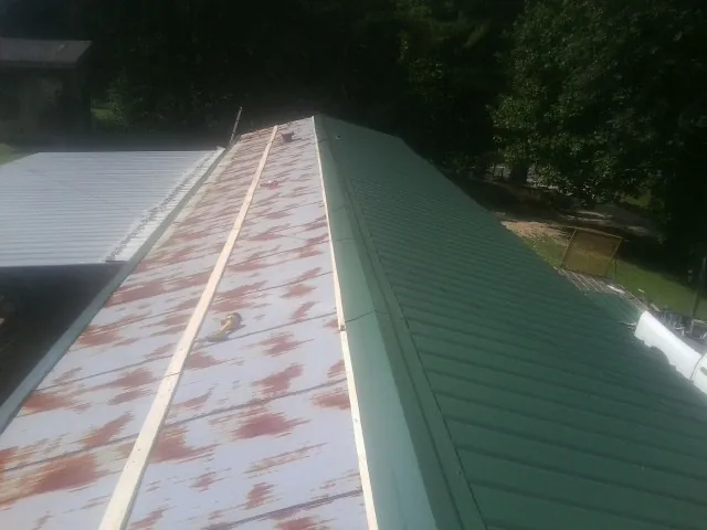Old rusted panels beside newly installed green metal roofing — Wind Damage Roof Repair by Roofing Brothers in Petoskey