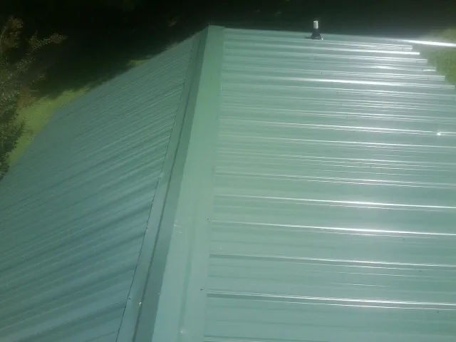 New green metal panels meeting at the ridge of a roof — Flat Roof Repair work by our crew in Petoskey