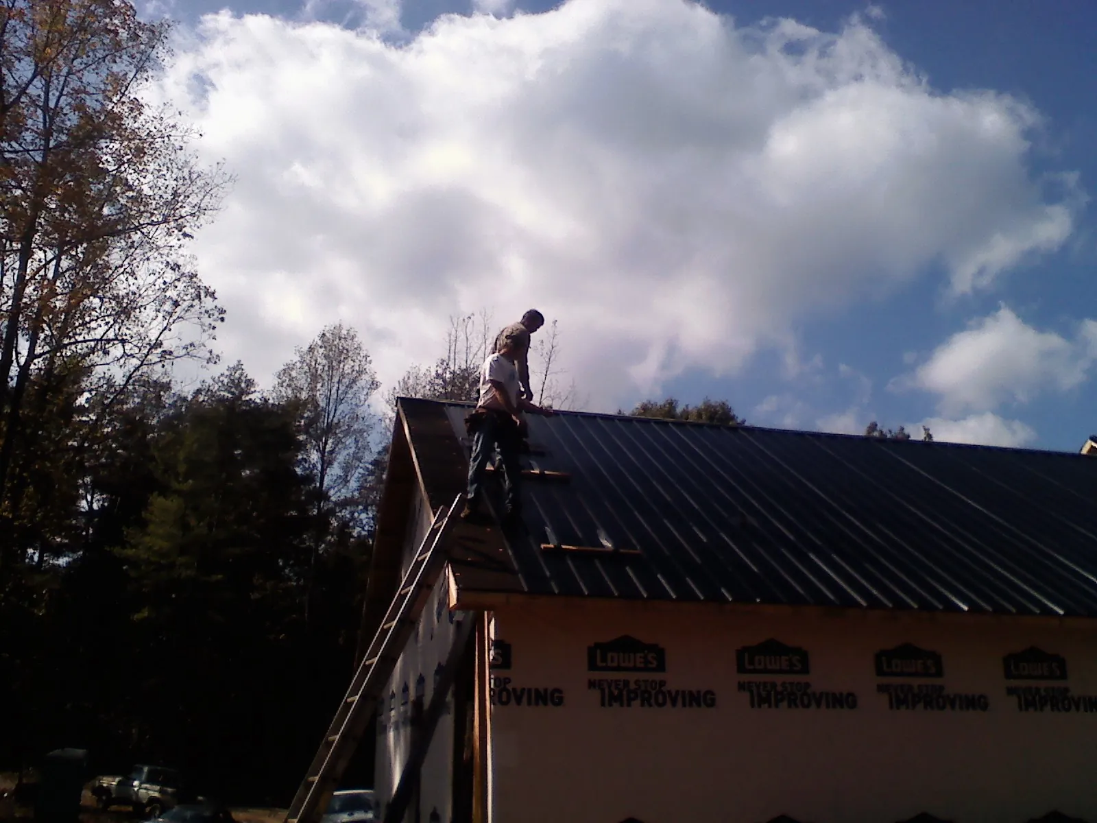 Roofer fastening dark metal panels high against a cloudy sky, from a Roof Inspection job in Petoskey