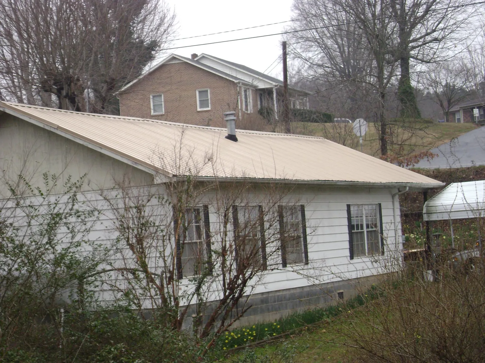 Tan metal roof on a white sided house set into a hillside — Commercial Roofing by Roofing Brothers in Petoskey