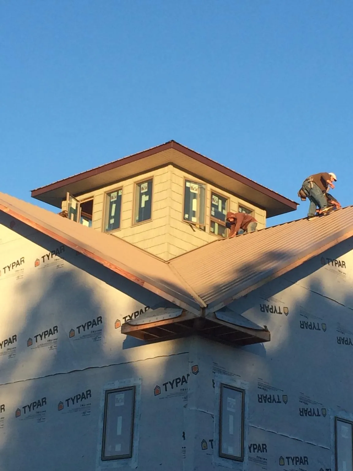 Roofers working around a rooftop cupola on a new metal roof at sunset — Roof Waterproofing in Petoskey by Roofing Brothers